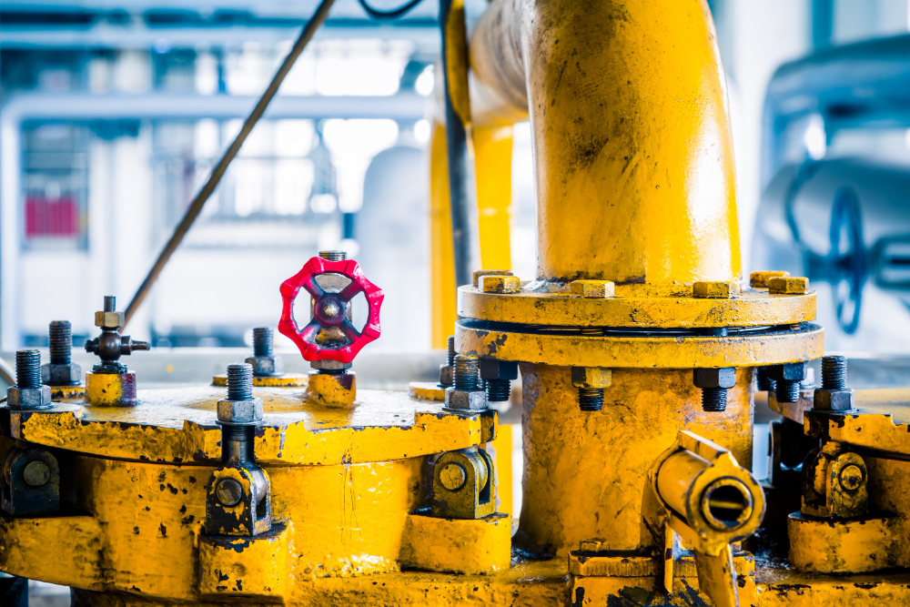 Industrial yellow valve assembly with a red handwheel and multiple bolts in a factory setting.