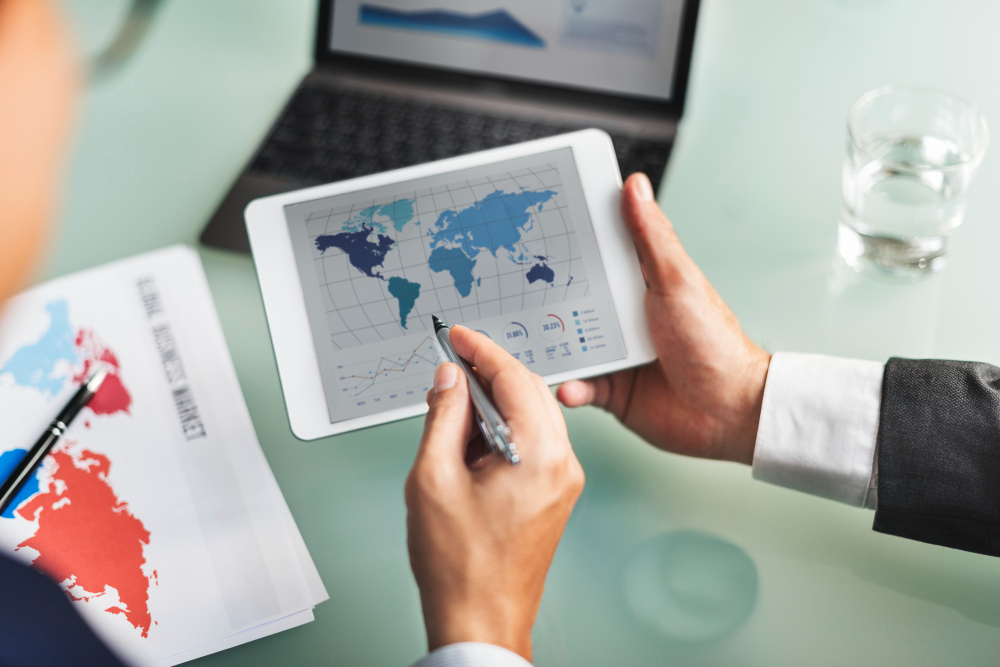 772927 - Ledesma International | Realidad Económica Person in a suit holds a tablet displaying a world map and charts during a data analysis meeting.