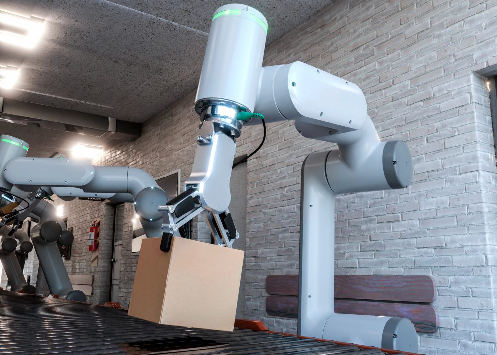 777471 - MeetThings | Realidad Económica Industrial robotic arm lifting a cardboard box over a conveyor belt in a lab-like setting with brick walls and bright lights.