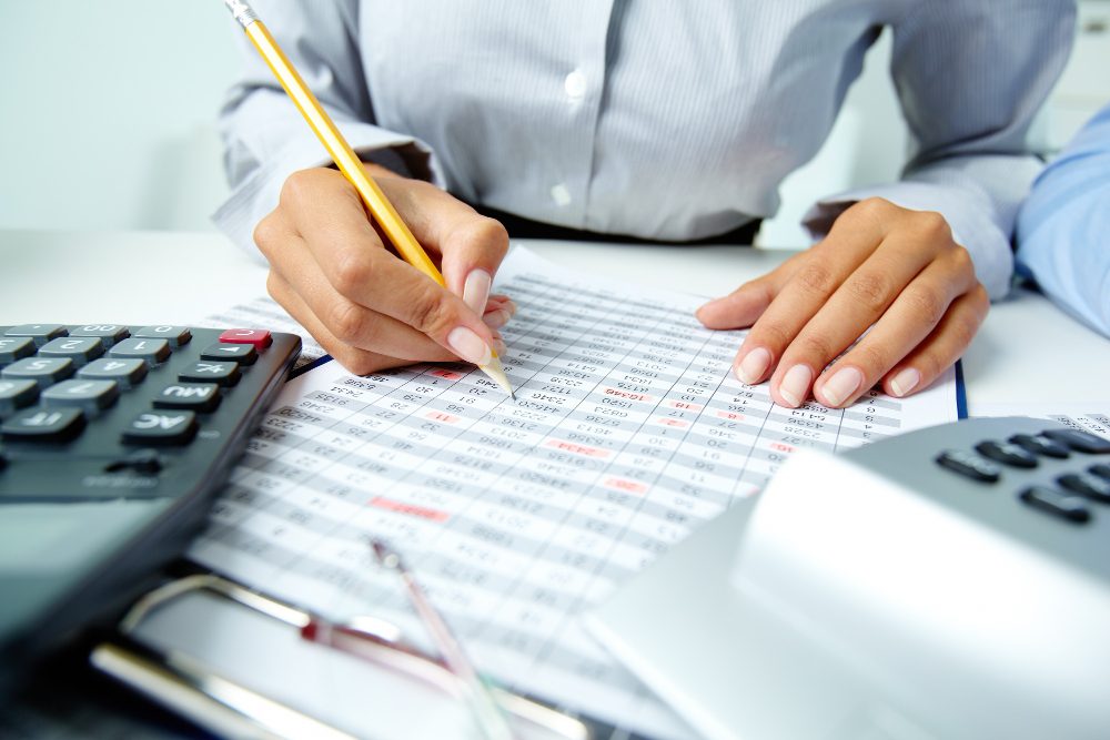 778603 - Lex Beckham | Realidad Económica Person uses a pencil to annotate a financial spreadsheet with a calculator nearby, on an office desk.