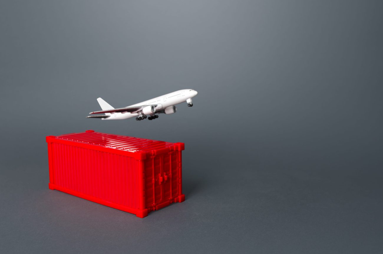 780630 IAS Handling | Realidad Económica White toy airplane lifting off from a red plastic crate against a gray backdrop.