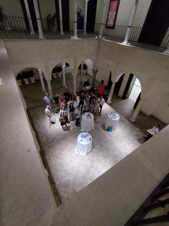 CAEM - Univ Lleida - IP | Realidad Económica Group of people gathered in a courtyard with arches, photographed from a balcony above during a social event.